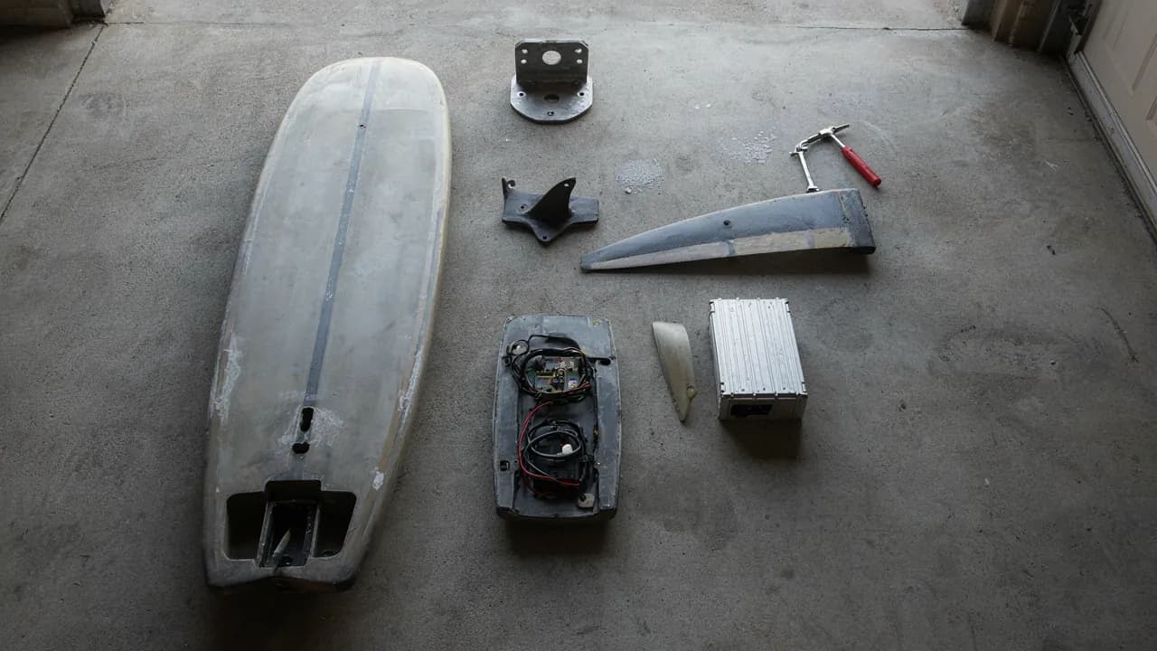 E-foil d’occasion entièrement démonté sur le sol d’un garage : planche, caisson ouvert, platine de mât, aile, fuselage et batterie séparés